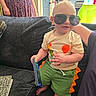 Kaleb joined the competition — help win amazing prizes! child, toddler, baby, sunglasses, smiling, portrait, couch, indoors, home, kitchen, family, tablet, toy, dinosaur_costume, green_shorts, orange, seated, barefoot, adult, broom
