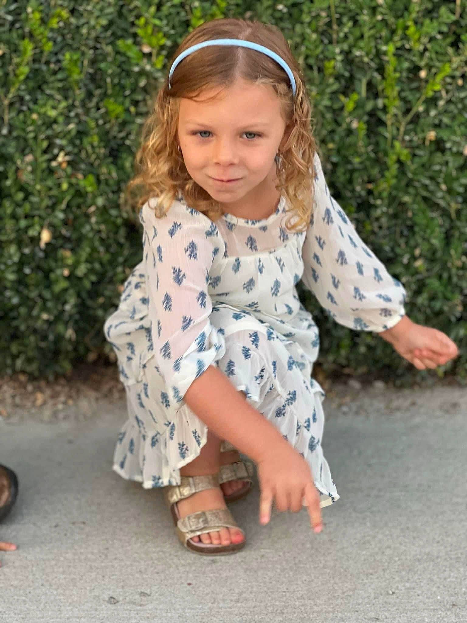 Ryleigh is registered to the contest to win money with this photo: baby_toddler_clothing, blond, child, day_dress, dress, foot, grass, hairstyle, happy, human_leg, joy, leisure, pattern, person, plant, road_surface, sandal, sitting, sleeve, smile