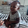 toddler, child, smiling, bed, blanket, dresser, basket, hand, room, television, clothing, furniture, indoor, person, happy, curly_hair, sitting, baby, home, cozy