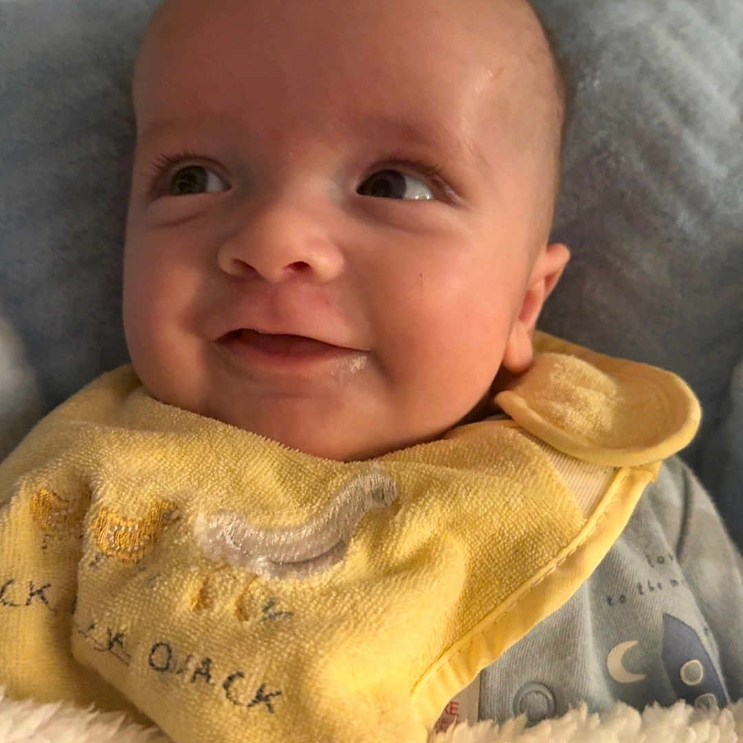 Noah joined the competition — help win amazing prizes! baby, blanket, child, closeup, clothing, cozy, cute, expression, face, happy, head, indoor, infant, newborn, portrait, skin, sleepwear, smiling, soft_texture, yellow_bib