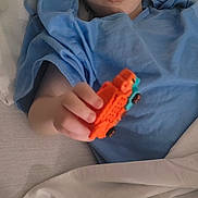 Waylon is registered to the contest to win money with this photo: child, bed, blue_shirt, toy_car, orange_toy, blanket, curious_expression, indoor, person, young_child, light_skin, short_hair, bedroom, bedding, lying_down, hand, focus, casual_clothing, relaxed, play