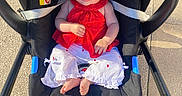 Rose a rejoint le concours — aidez-le/la à gagner de superbes lots ! baby, stroller, red_clothing, white_pants, infant, child, person, outdoor, sunlight, footwear, jeans, pavement, handlebar, black_stroller, curious_expression, seated, safety_belt, closeup, daylight, portrait