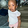 Damira is registered to the contest to win money with this photo: blanket, casual_clothing, child, earrings, expression, face, fan, flooring, furniture, hair_beads, indoor, person, pink_shorts, portrait, socks, standing, toddler, white_top, wooden_floor, young_child