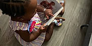 Damira joined the competition — help win amazing prizes! toddler, child, braids, hair_bow, dress, striped_clothing, book, reading, floor, wooden_floor, sandals, indoor, sitting, finger_pointing, young_child, cute, colorful, playroom, engaged, casual