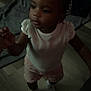 Damira joined the competition — help win amazing prizes! beads, braided_hair, child, curious, cute, dim_lighting, floor, flooring, home, indoor, infant, patterned_shorts, person, portrait, socks, standing, toddler, white_top, wooden_floor, young_child