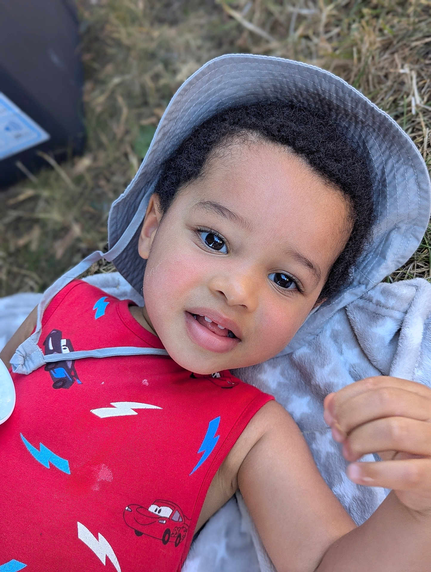 Maé participe au concours pour gagner de l'argent avec cette photo : child, toddler, boy, face, hat, red_clothing, cartoon_print, outdoor, grass, blanket, portrait, smiling, cute, baby, headwear, casual_clothing, daylight, skin, hand, expression