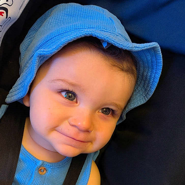 Kian is registered to the contest to win money with this photo: baby, baby_fashion, blue_clothing, blue_hat, child, closeup, cute, expression, eyes, face, headwear, indoor, infant, person, portrait, seatbelt, skin, smile, toddler, young_child