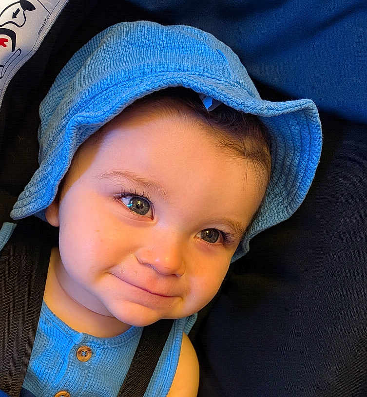 Kian is registered to the contest to win money with this photo: toddler, child, baby, blue_hat, blue_clothing, smile, face, eyes, cute, portrait, headwear, infant, closeup, young_child, person, seatbelt, indoor, skin, expression, baby_fashion