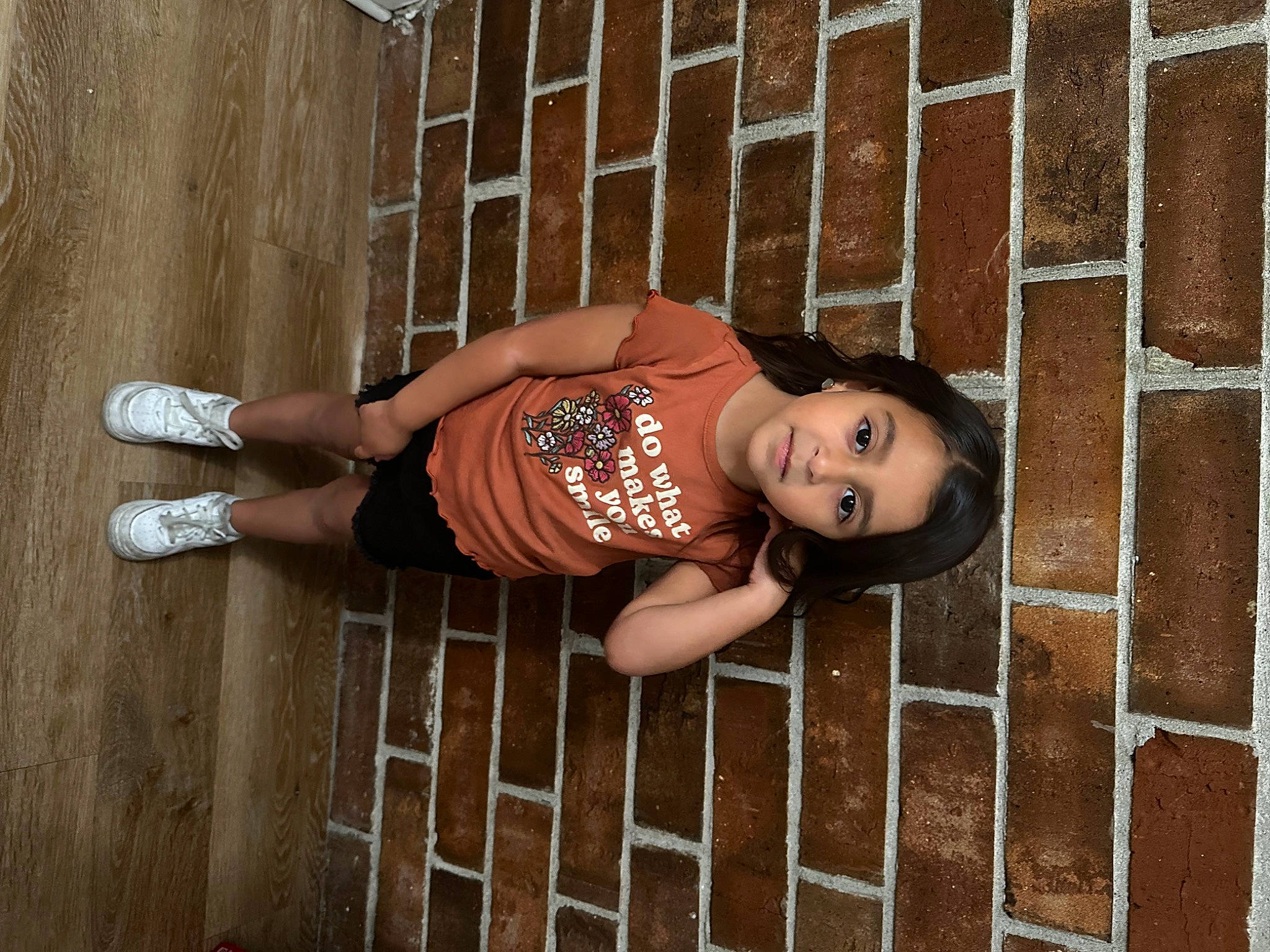 Selena is registered to the contest to win money with this photo: brick, brickwork, child, cool, dress, face, flash_photography, human_leg, knee, leg, pattern, person, portrait_photography, sitting, t_shirt, textile, thigh, toddler, visual_arts, waist