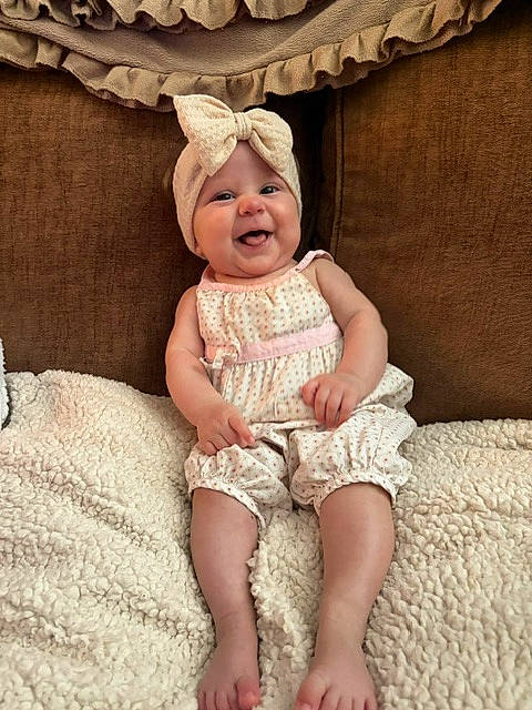 Brynlee Dallas is registered to the contest to win money with this photo: baby, barefoot, blanket, bow, brown_background, child, cushion, cute, dress, female, happy, headband, indoor, infant, outfit, photography, portrait, sitting, smiling, textile