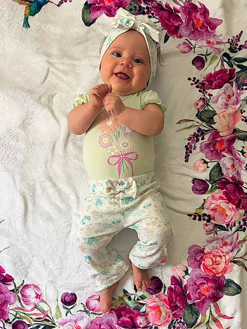 baby, child, close_up, clothing, colorful, feet, floral_blanket, flowers, hands, happy, headband, indoor, infant, lying_down, onesie, pants, photography, pink_flowers, portrait, smiling