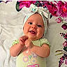 baby, child, infant, smiling, happy, lying_down, portrait, face, headband, bow, floral, blanket, bedding, indoor, close_up, green_clothing, baby_clothes, hands, playful, adorable