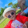 Mya a rejoint le concours — aidez-le/la à gagner de superbes lots ! toddler, child, sunglasses, hat, red_jacket, strawberry_pattern, outdoor, grass, picnic, summer, sunny, blue_sky, tree, fence, person, casual_clothing, baby, nature, playful, fun