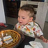 child, boy, birthday, pie, candle, toy, van, table, chair, shirt, animal_print, spiky_hair, napkin, indoor, celebration, food, cute, smiling, happy, person