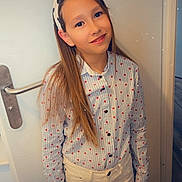 Lea a rejoint le concours — aidez-le/la à gagner de superbes lots ! child, girl, smiling, standing, long_hair, shirt, heart_pattern, white_pants, door, door_handle, indoor, casual, portrait, person, young, headband, floor, wall, happy, fashion