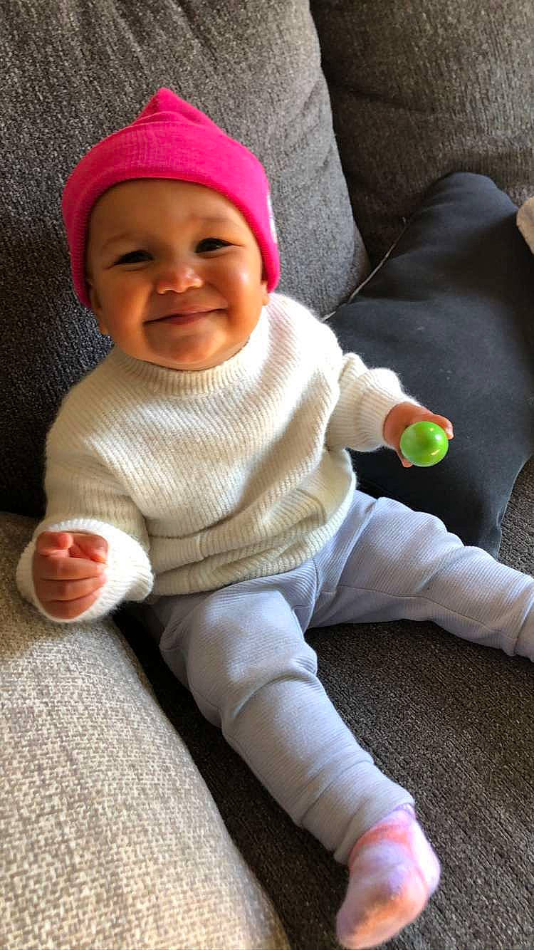 Soleil is registered to the contest to win money with this photo: baby, baby_toddler_clothing, cap, cheek, comfort, eye, face, flooring, happy, head, headwear, human_body, joy, knit_cap, lap, leg, person, skin, sleeve, smile
