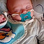 baby, sleeping, pacifier, nasal_tubes, blanket, bib, pillow, smile, cozy, infant, cute, resting, indoors, child, face, clothing, soft, comfort, healthcare, peaceful