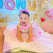 True is registered to the contest to win money with this photo: baby, child, birthday, pink, dress, smiling, crawling, flower_headband, blanket, balloon, decorations, indoor, happy, celebration, face, person, carpet, cute, party, toddler