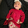 baby, child, infant, red_dress, headband, bow, smile, tongue_out, patterned_leggings, cherry_pattern, black_blanket, cute, happy, indoors, portrait, person, lying_down, young_child, cozy, clothing