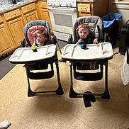 Oaklynn joined the competition — help win amazing prizes! baby, high_chair, cupcake, kitchen, counter, cabinet, floor, baby_bottle, water_bottle, trash_can, toy, person, food, appliance, window, floor_tile, expression, seat, tabletop, indoor