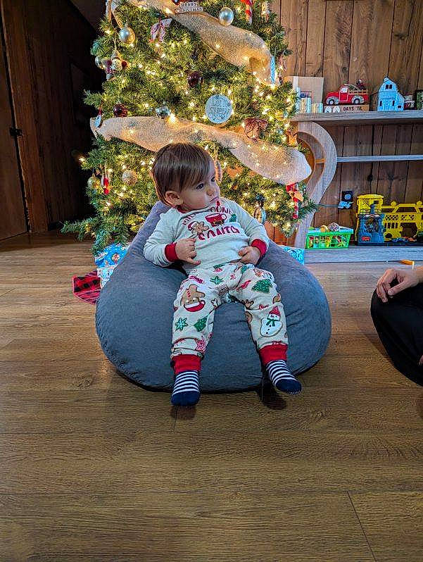 John is registered to the contest to win money with this photo: baby_toddler_clothing, child, christmas, christmas_decoration, christmas_eve, christmas_ornament, christmas_tree, conifer, event, fun, holiday, holiday_ornament, interior_design, lap, ornament, person, plant, room, sitting, toddler