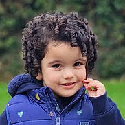 Isla joined the competition — help win amazing prizes! child, curly_hair, smile, blue_jacket, outdoor, green_background, cute, portrait, young_child, happy, fashion, winter_clothing, face, person, nature, park, casual_wear, innocence, warm_clothes, kid