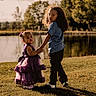 blue_shirt, casual_clothing, child, children, curly_hair, dress, grass, holding_hands, lake, nature, outdoor, park, portrait, purple, shadow, sibling, sunlight, toddler, trees, water