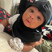 Sevynn joined the competition — help win amazing prizes! baby, infant, child, portrait, close_up, face, eyes, wide_eyed, looking_at_camera, black_bonnet, black_clothing, socks, heart_pattern, cushion, indoor, home, seated, adorable, photography, baby_fashion