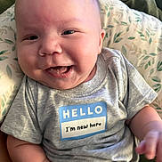 Cameron joined the competition — help win amazing prizes! baby, infant, child, smiling, happy, portrait, face, eyes, mouth, gray_shirt, sticker, hello, newborn, sitting, pillow, blanket, bed, indoor, closeup, photography