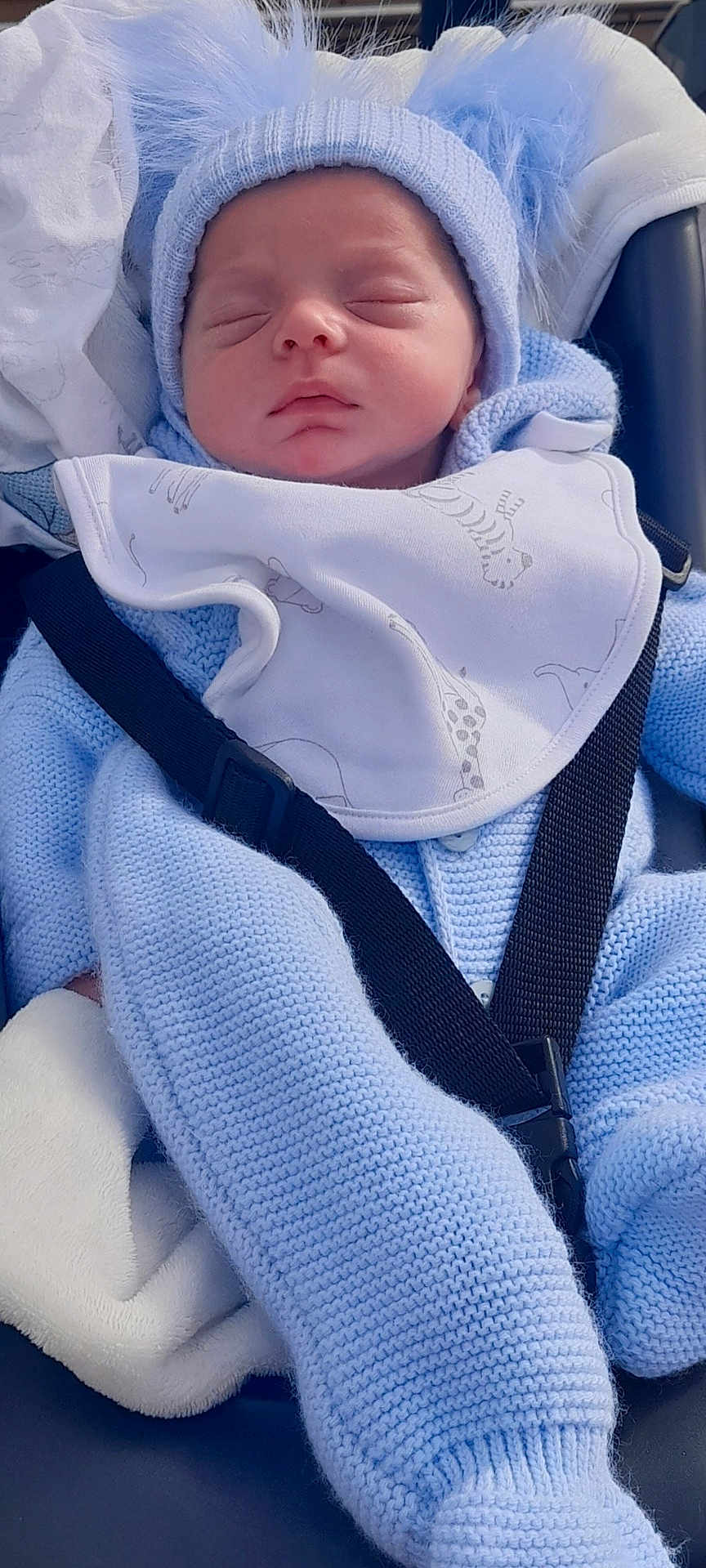 Jaxon is registered to the contest to win money with this photo: baby, sleeping, blue_hat, knitwear, car_seat, baby_bib, baby_clothing, infant, peaceful, child, cute, pom_poms, blanket, seatbelt, portrait, face, young_child, indoors, soft_texture, cozy