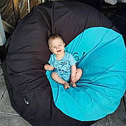 Gabriel a rejoint le concours — aidez-le/la à gagner de superbes lots ! baby, child, bean_bag, blue_clothing, outdoor, happy, smiling, sitting, floor, stone_tiles, wooden_wall, chair, furniture, person, casual, relaxed, infant, comfort, seat, sunlight