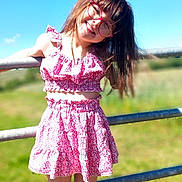 Lilia a rejoint le concours — aidez-le/la à gagner de superbes lots ! child, girl, smile, glasses, pink_clothing, dress, sunny, outdoor, fence, grass, blue_sky, happy, playful, summer, fashion, portrait, young, nature, casual, daylight