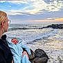 woman, baby, ocean, waves, rocks, sunset, clouds, sky, water, person, holding, outdoor, nature, portrait, glasses, hair_bow, clothing, rocky_shore, infant, calm
