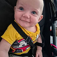 Henry is registered to the contest to win money with this photo: baby, child, smiling, blue_eyes, yellow_shirt, stroller, seatbelt, cute, infant, happy, portrait, closeup, person, sitting, casual_clothing, indoors, young_child, face, hand, playful