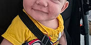 Henry is registered to the contest to win money with this photo: baby, child, smiling, blue_eyes, yellow_shirt, stroller, seatbelt, cute, infant, happy, portrait, closeup, person, sitting, casual_clothing, indoors, young_child, face, hand, playful