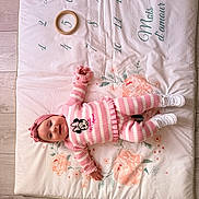 Gina participe au concours pour gagner de l'argent avec cette photo : baby, child, pink_clothing, striped_outfit, headband, smiling, lying_down, playmat, floral_pattern, numbers, wooden_floor, white_shoes, cute, infant, person, indoor, soft_mat, toy_ring, happy, portrait