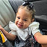 baby, bow, car, car_seat, child, closeup, hair_bow, happy, indoors, infant, pacifier, patterned_clothing, portrait, ruffled_sleeves, seatbelt, sitting, smiling, toy, vehicle, white_shirt
