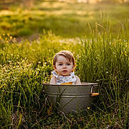 Rory is registered to the contest to win money with this photo: toddler, child, bucket, grass, field, outdoor, sunlight, nature, greenery, portrait, baby, daylight, summer, young_child, cute, innocent, metal_bucket, curious, sitting, golden_hour