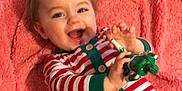 Rory is registered to the contest to win money with this photo: baby, smiling, striped_pajamas, toy, blanket, indoor, child, happy, infant, cute, lying_down, soft_texture, holiday_theme, playful, young_child, face, hand, cushion, pajamas, fun