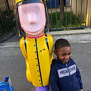 élia a rejoint le concours — aidez-le/la à gagner de superbes lots ! child, boy, hoodie, smile, outdoor, playground, statue, colorful, yellow, purple, sidewalk, fence, casual_clothing, person, urban, daylight, happy, standing, toy_figure, metal