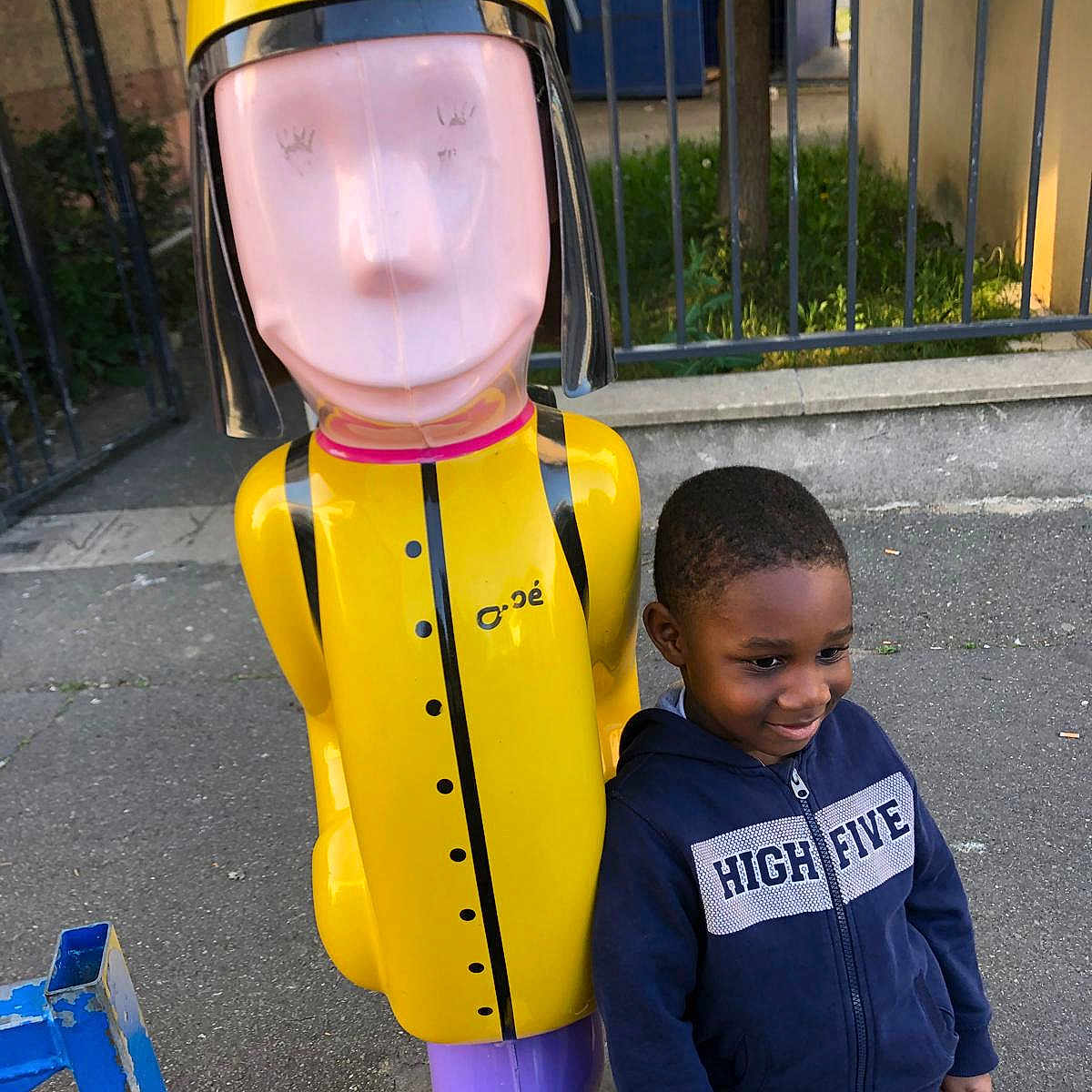 élia a rejoint le concours — aidez-le/la à gagner de superbes lots ! child, boy, hoodie, smile, outdoor, playground, statue, colorful, yellow, purple, sidewalk, fence, casual_clothing, person, urban, daylight, happy, standing, toy_figure, metal
