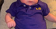 Jettson is registered to the contest to win money with this photo: baby, infant, child, polo_shirt, purple_clothing, denim_jeans, couch, pillow, indoor, person, face, head, sitting, furniture, window, home, casual_clothing, expression, soft_lighting, relaxing