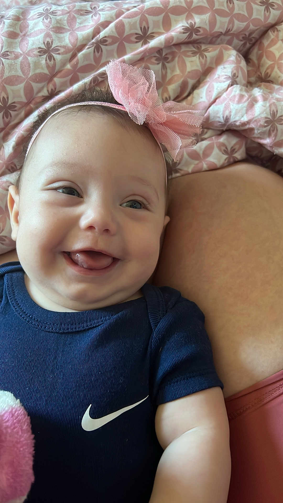 Zurriah is registered to the contest to win money with this photo: baby, smiling, headband, pink_bow, onesie, navy_blue_clothing, blanket, patterned_blanket, face, cheek, happy, tongue_out, infant, skin, closeup, lying_down, human, cute, indoors, soft_toy