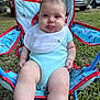 baby, child, outdoor, grass, chair, onesie, bib, tongue, playful, cute, person, infant, summer, seat, legs, sock, parked_cars, daylight, expression, cute_face