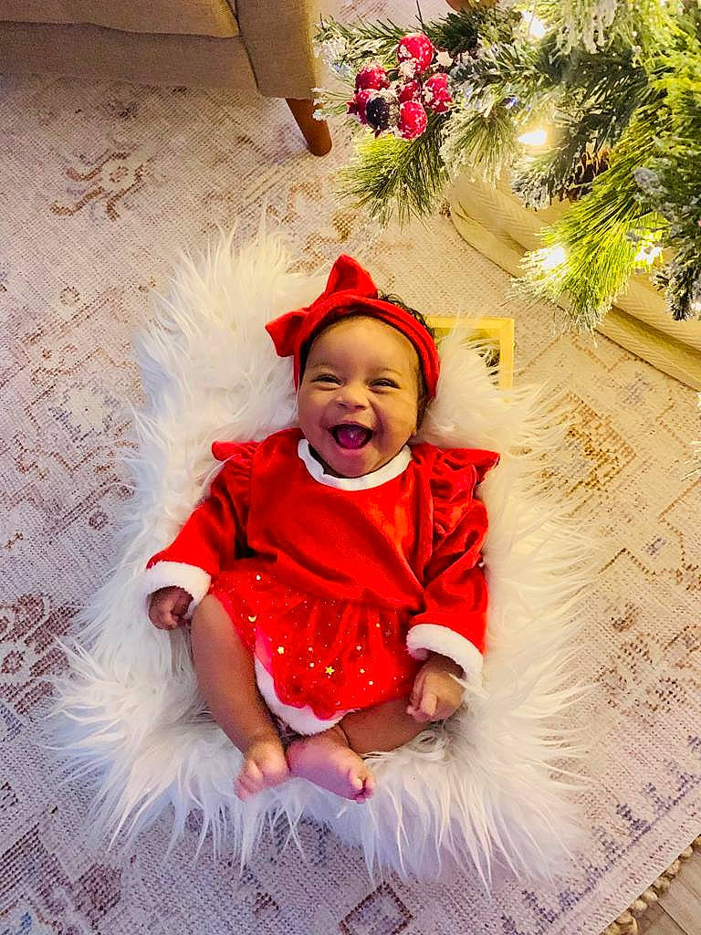 Leila is registered to the contest to win money with this photo: baby, baby_toddler_clothing, child, christmas_ornament, dress, event, facial_expression, flower_arranging, fun, grass, happy, headwear, holiday, ornament, person, pink, plant, red, smile, toddler