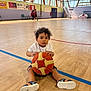 toddler, child, basketball, gym, sports, court, indoor, shoes, curly_hair, white_shirt, blue_shorts, sandals, wooden_floor, windows, natural_light, basketball_hoop, kids, people, walking, sportswear