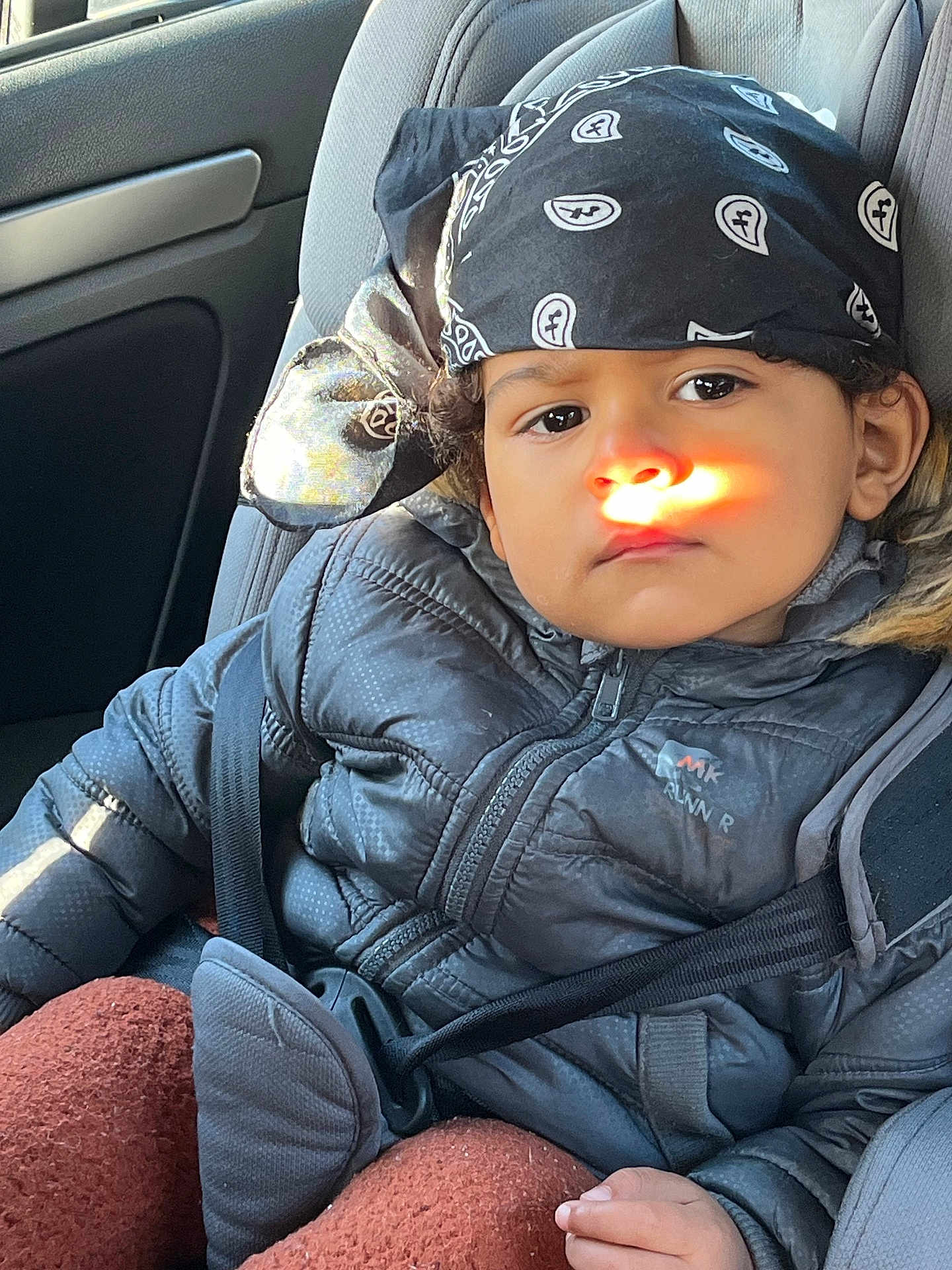 Ilyan participe au concours pour gagner de l'argent avec cette photo : child, car_seat, seatbelt, bandana, jacket, sunlight, face, window, car_interior, hand, curly_hair, expression, warm_clothing, safety, portrait, indoor, casual, seat, person, young