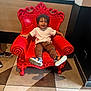 Ilyan a rejoint le concours — aidez-le/la à gagner de superbes lots ! toddler, child, red_chair, curly_hair, indoor, happy, smiling, white_tshirt, brown_pants, blue_sandals, floor_tiles, woman, phone, furniture, portrait, casual, light, window, shadow, decor