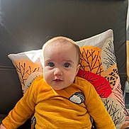 Joséphine a rejoint le concours — aidez-le/la à gagner de superbes lots ! baby, child, face, eyes, clothing, yellow_top, sitting, cushion, patterned_pillow, leaf_pattern, indoor, furniture, leather_chair, cute, portrait, infant, young_child, expression, natural_light, casual