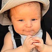 Seferino is registered to the contest to win money with this photo: baby, infant, child, portrait, face, hat, sun_hat, sitting, hands, clasped_hands, smiling, cute, harness, carrier, clothing, indoor, close_up, photography, dark_background, safe